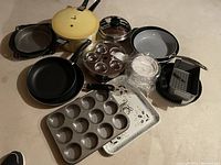 Overview of all cookware and bakeware items in the lot, showing frying pans, baking sheets, muffin pan, crock pot, and pressure cooker.