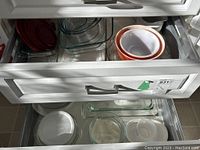 Drawers with stacked clear and white glass Pyrex bowls, storage containers with red lids, and casserole dishes.