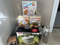 Photo of seized kitchen appliances boxed and loose on floor including salad spinner, juicers, multi-grater, dressing bottles, salt and sugar shakers.
