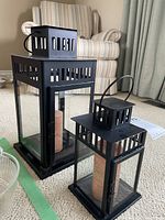 Angle showing both black metal lanterns with beige candles inside placed on carpet