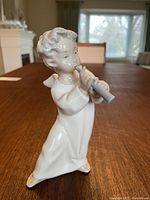 Front view of the angel figurine playing the flute, showing detailed face and gown folds.
