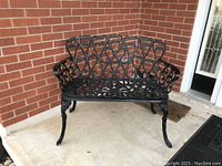 Front view of black decorative metal outdoor bench showing ornate backrest, seat, and armrest scrollwork, and curved legs.