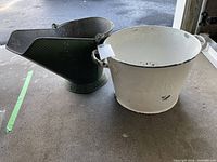 White metal bucket stamped APEX with handles beside a green metal coal scuttle on concrete floor.