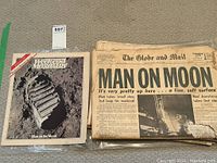Overall view of two newspapers and one magazine laid out showing the headline 'MAN ON MOON' and the Weekend Magazine cover with astronaut footprint.