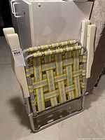 Two folded aluminum frame outdoor chairs with yellow, white, and gray woven mesh straps, folded flat leaning against a wall.
