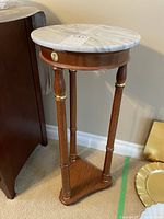 Full side view of the wooden plant stand showing the legs, brass accents, and marble top with the crack taped.