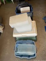 Photo showing multiple large plastic bins in blue with several lids stacked on top, both translucent and solid color lids.