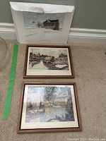 Photo of two framed prints on the floor with one unframed print in a protective sleeve leaning against the wall.