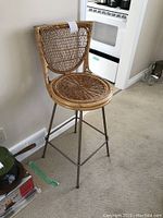 Side and partial front view of the rattan bar stool showing woven seat and backrest, metal frame, and swivel base