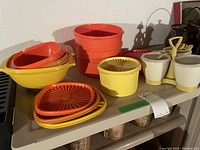 Full set of retro Tupperware items including stacking bowls, lids, condiment set, plastic cups, and pitchers shown on shelf.
