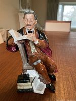 Side view of the sitting figurine of a professor reading a book, detailing the colors and pose.