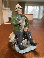 Photo of Royal Doulton fisherman figurine sitting on log, holding a fish, angled front left side view.