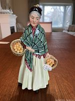 Front view of Royal Doulton porcelain figurine The Orange Lady holding two baskets of oranges.