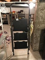 Front view of the Cosco step ladder showing three black plastic steps with textured surfaces and foam padded handle on metal frame.