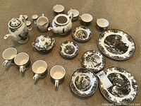 Top view of entire Johnson Bros. The Friendly Village china set with plates, bowls, cups, mugs, teapots, sugar bowl, creamer, and egg holders arranged on the floor.