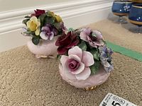 Two porcelain floral bouquets with pink decorative bases and multicolored flowers.