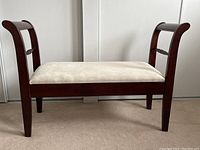 Front view of wooden bench with cushioned white patterned seat and curved wooden arms.