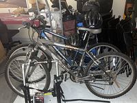 Two adult mountain bikes, Iron Horse Axion and Matrix Atashi, positioned indoors with visible wear, one with a blue and silver frame and one with black and silver.