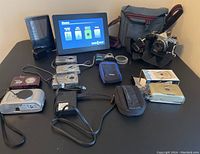 Overview of all cameras, Nikon SLR, picture frame, bags, cables on table