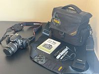 Overview of camera with attached lens and strap, battery charger, USB cable, lens cap holder, instruction manual, LensPen pens, memory cards, and Golla camera bag
