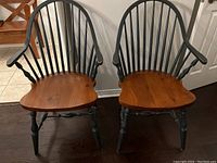 Front view of two vintage Windsor captain chairs side by side showing black spindle backs and natural wood seats.
