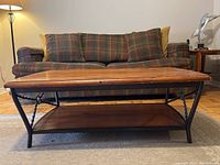 Front view of the coffee table showing wood top and metal frame with twisted detail, placed in front of a plaid couch.