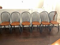 Six chairs in a row against a white wall on hardwood floor