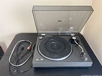 Full view of black turntable with rubber mat platter, tonearm, speed buttons, and dust cover, placed on black surface.