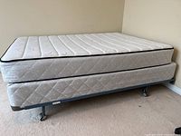 Full view of full/double white Sealy Posturepedic mattress on boxspring resting on metal frame with wheels, placed in bedroom corner.