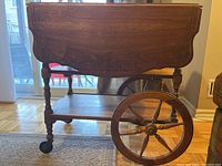 Front view showing drop leaf closed, carved edge detail, spindle legs and large spoked rear wheel