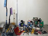 Wide view of assorted paint and hardware supplies including brushes, cans, and tools on table with white wall background.