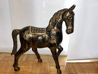 Full side profile of the black carved wooden horse with glass and mirror adornments on saddle and neck.