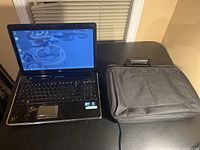 Full view of HP Pavilion laptop next to black Samsonite soft laptop case on a dark table.