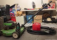 Side view of green Lawn Boy lawnmower with gas can and garden hose coiled on floor nearby. Storage items in background.