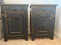 Pair of black distressed wood vintage French nightstands side by side showing drawer and cupboard door with scalloped base