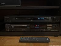 Sony DVD player DVP-NS315 on top, with front panel and LED display showing 'NO DISC'. Below it, Sony CD player CDP-70 showing digital display and control buttons. Remote control is placed on shelf below the players.
