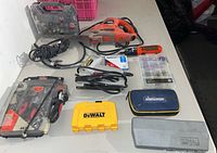 Tools laid out on white table: Black & Decker jig saw, screwdriver, accessory bit cases, and Stanley electric stapler