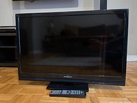 Front view of the 26 inch Insignia LCD TV with remote control resting on the base.