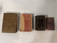 Four antique books laid flat showing front covers, colors brown, red/beige, black with gold detailing, and purple titled 'Mary Queen of Scots'