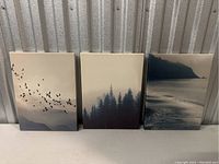 Three canvas art pieces side by side showing different nature scenes: birds flying over mountains, pine forests, and sea coastline.