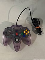 Front view of the Atomic Purple Nintendo 64 controller showing translucent plastic shell, buttons, analog joystick, and cable coiled and secured with an orange rubber band.