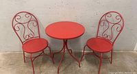 Wide shot of red metal bistro table and two matching chairs showing overall set condition and design.