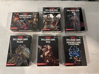 Photo showing all seven sealed D&D card packs with clear titles and artwork: Monster Cards Volo's Guide to Monsters, Spellbook Cards Martial Powers & Races, Bard, Paladin, Druid, Xanathar's Guide to Everything.