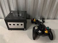 Nintendo GameCube console and black wired controller on table showing front and top details.