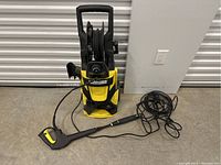 Full view of the Karcher power washer showing hose reel, power cord, and spray gun placed on the floor to the right side.