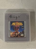 Nintendo Gameboy Metroid II: Return of Samus cartridge in clear plastic protective case with handwriting on the cartridge's upper edge