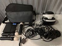Overview of the VR headset, 3 Play Station Move motion controllers, PlayStation camera, cables, and carry bag arranged on a table.