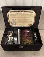 Photo of the open collector's box showing the Ryu figurine, art cards, and black cloth inside, with the 25th Anniversary plaque attached to the lid.