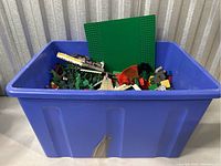 Full view of blue storage bin filled with assortment of vintage LEGO pieces including baseplates and partial models.