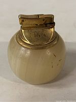 Front view of vintage marble table lighter showing cream-colored marble base and brass lighter mechanism top with wear marks.